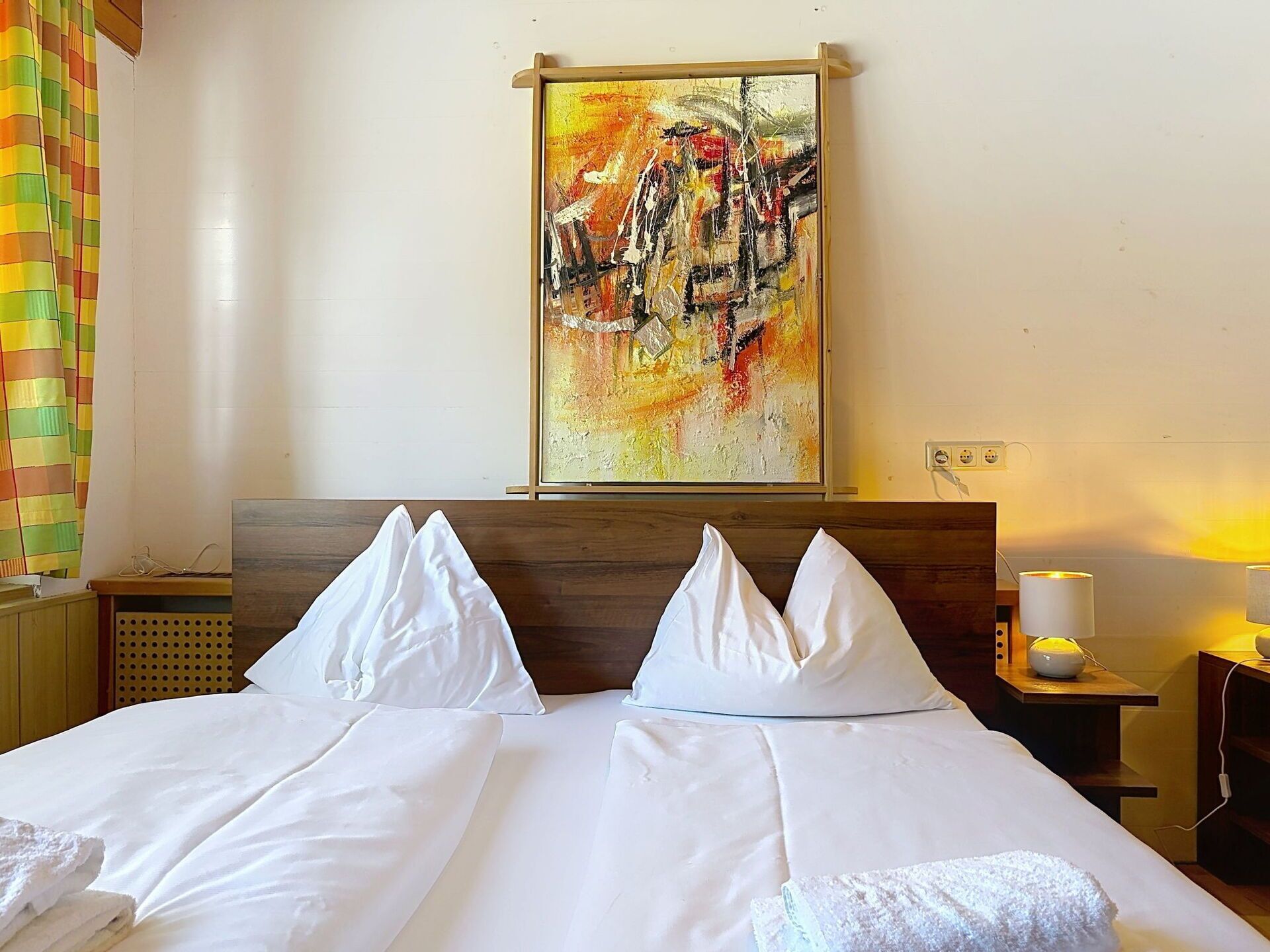 Een hotelkamer met een bed, kussens, een schilderij aan de muur en een nachtkastje met een lamp.