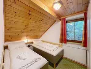 Ein Zimmer mit zwei Betten, einem Vorhangfenster und einer Holzbalkendecke.