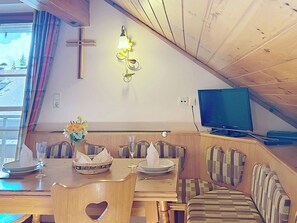 Ein Essbereich mit einem Holztisch, Bänken und einem Fernseher auf einem Standfuß.