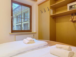 Een slaapkamer met een bed, een raam, een radiator en een houten garderobe met kledinghangers.