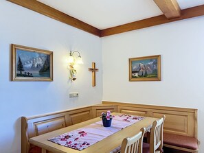 Een eetruimte met een houten tafel, bankjes en twee schilderijen aan de wand.