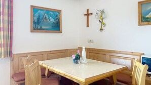 A dining area with a wooden table and chairs, a cross on the wall, and a painting of mountains. - Nice apartment for 6 people with WIFI, TV, balcony and pets allowed (St Michael Im Lungau)