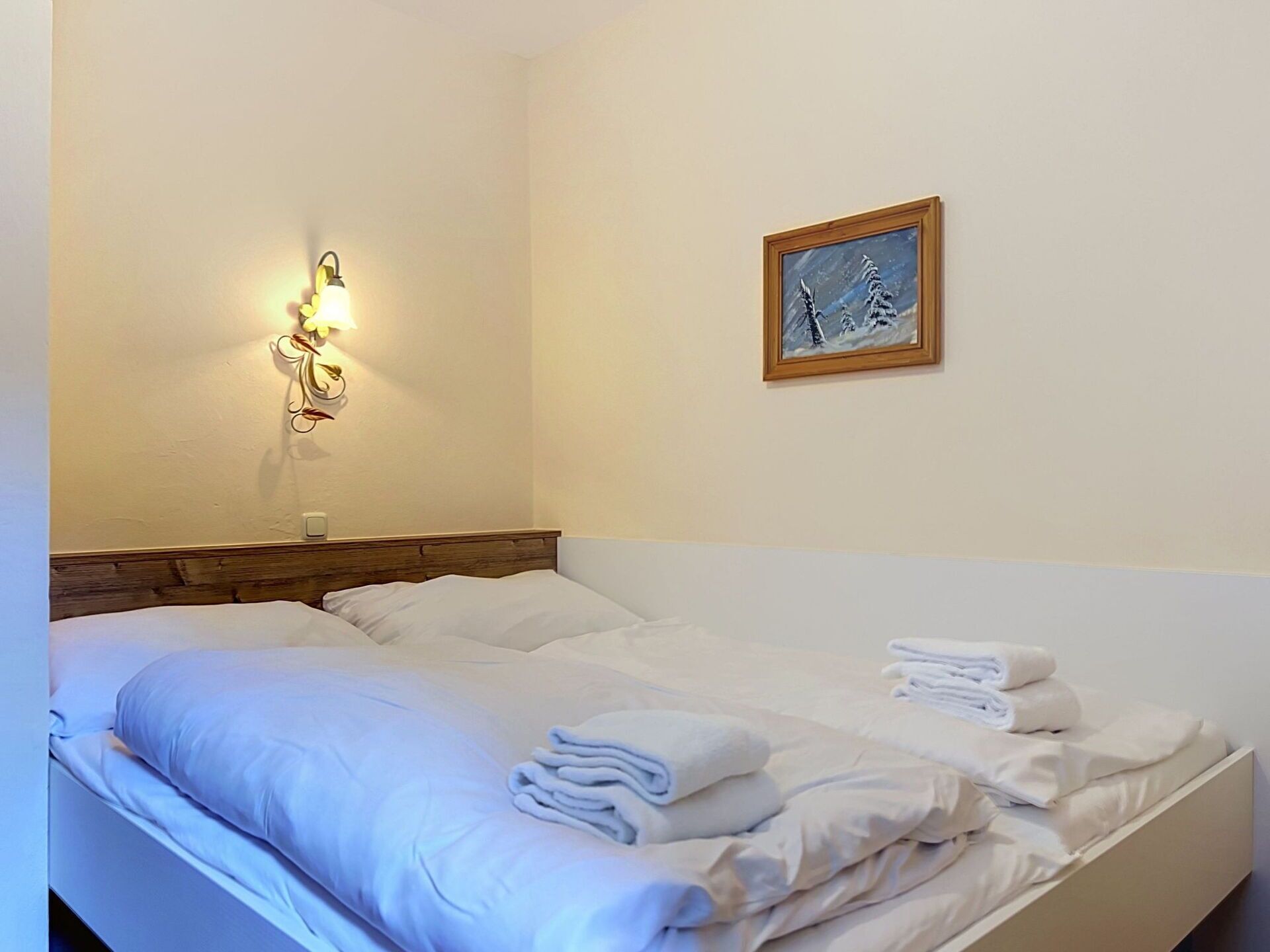 Quarto de hotel com cama, luminária fixada na parede e quadro emoldurado.