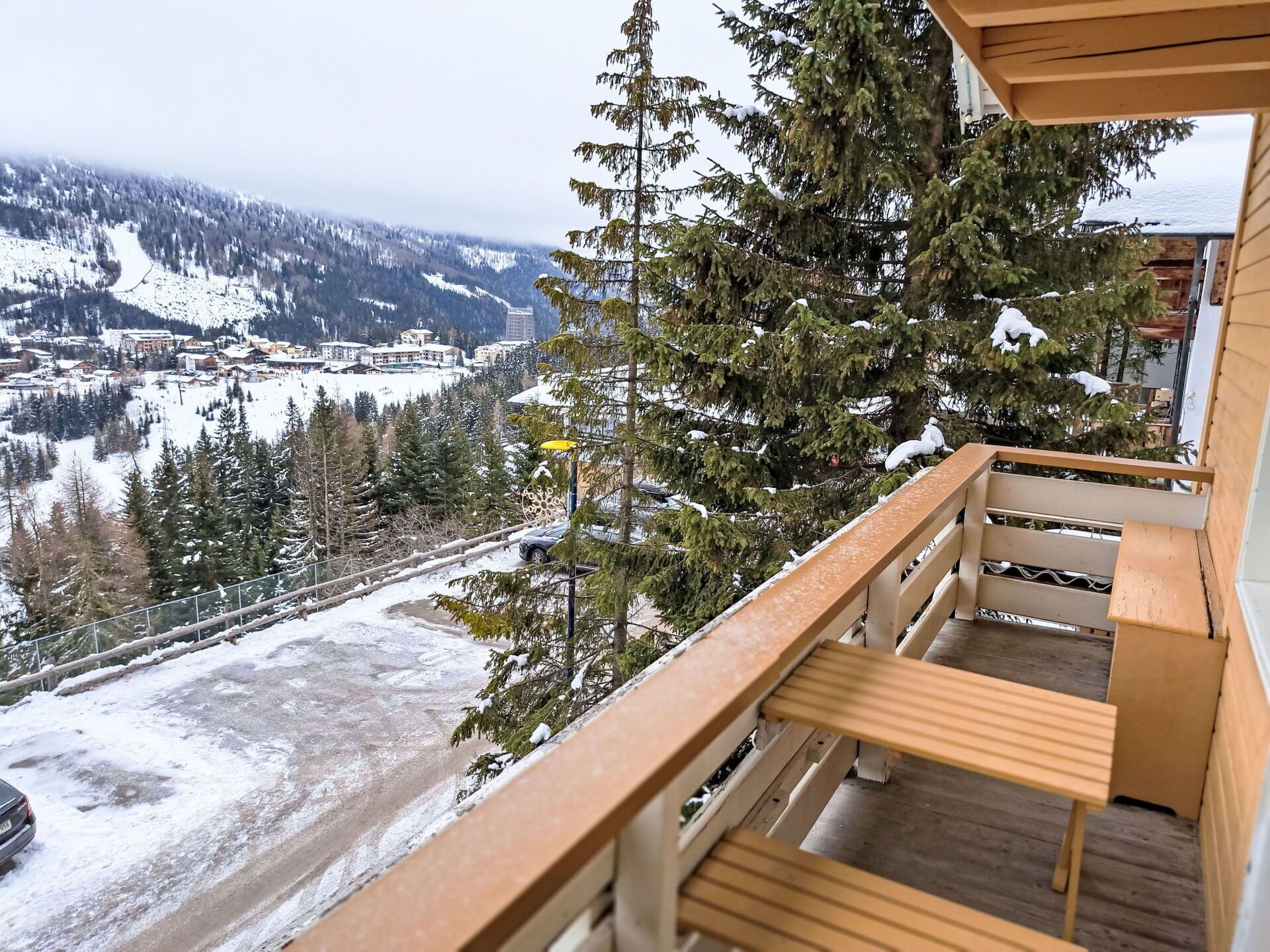 Een balkon met uitzicht op een besneeuwd berglandschap, inclusief een skigebied en een weg.