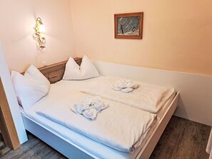 Ein ordentlich bezogenes Bett mit weißen Leinen und Handtüchern, ein hölzerner Kopfteil, eine Wandleuchte und ein gerahmtes Bild an der Wand.