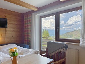 A room with a bed, a table, a chair, a TV mounted on the wall, and a window with a view of the outdoors. - Lovely apartment for 6 guests with WIFI, TV, balcony and pets allowed (St Michael Im Lungau)