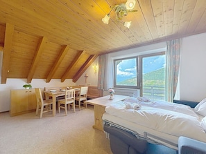 Ein Zimmer mit Holzboden, einem Bett, einem Schreibtisch und einem Fenster mit Bergblick.