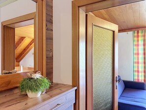 A room with a wooden ceiling, a large mirror, a wooden dresser with a plant, a blue sofa, and a door with a textured panel. - Nice apartment for 6 guests with WIFI, TV, balcony and pets allowed (St Michael Im Lungau)