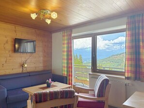 A cozy room with a wooden ceiling, a flat-screen TV mounted on the wall, a sofa, a table with a chair, and a window with a view of a mountainous landscape. - Nice apartment for 6 guests with WIFI, TV, balcony and pets allowed (St Michael Im Lungau)