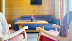 A cozy room with a wooden wall, a blue sofa, a wooden table, and two chairs. - Beautiful apartment for 6 guests with WIFI, TV, balcony and pets allowed (St Michael Im Lungau)