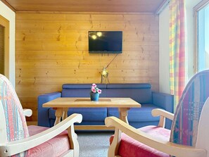 Ein gemütliches Zimmer mit einer Holzvertäfelung, einem blauen Sofa, einem Holztisch und zwei Stühlen.