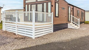 Une maison mobile avec une façade en bois, une terrasse blanche et un petit escalier menant à l’entrée.