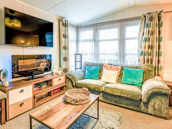 A living room with a sofa, a coffee table, a TV, and a window with curtains.