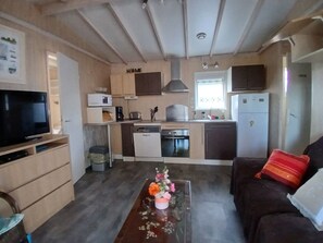 A compact living space with a kitchenette, a dining area, and a TV. - Cottage at a small 2** campground (Erdeven)
