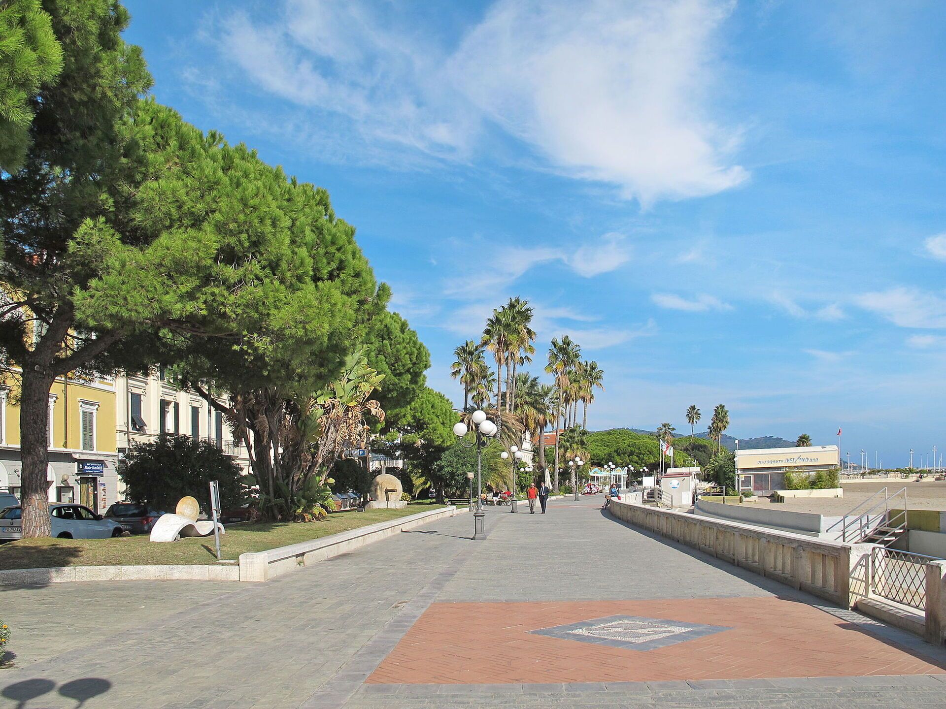 Un chemin pavé, bordé d’arbres et de palmiers, qui mène à un plan d’eau.