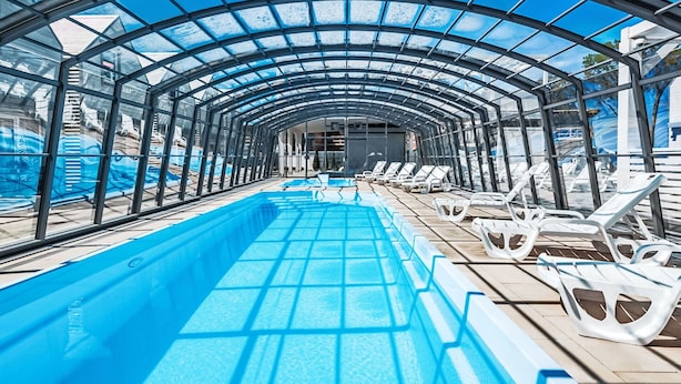 En indendørs swimmingpool med glasloft, liggestole og frit udsyn til himlen.