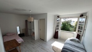 A bedroom with a bed, a wooden nightstand, a wardrobe, a radiator, and a window with a view of greenery outside. - Spacious house for large family or group - Near Villejuif Metro Line7 (Villejuif)