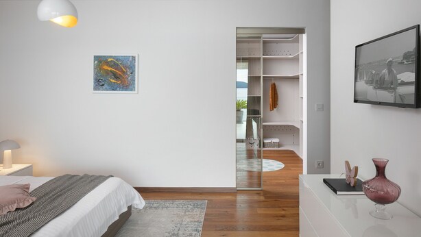 A modern bedroom with a bed, bedside lamp, artwork, and a view into a bathroom. - Stunning Villa With Pool in Sukosan (Sukosan)