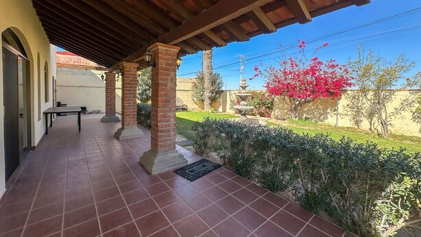 Ein überdachter Patio-Bereich mit Fliesenböden, Backsteinpfeilern und einer Bank.