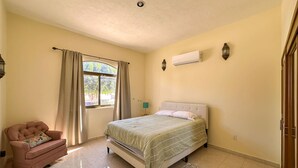 Ein Schlafzimmer mit Bett, Stuhl, einem fensterbepflanzten Fenster, einer Klimaanlage und einer Lampe.