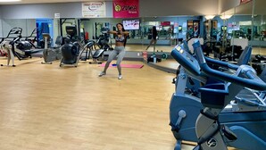 Et fitnesscenter med træningsudstyr, spejle og en kvinde, der træner.