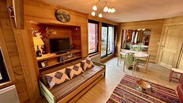 Ein gemütliches Holzhaus-Interieur mit einer Couch, einem Fernseher, einem Esstisch und Stühlen.
