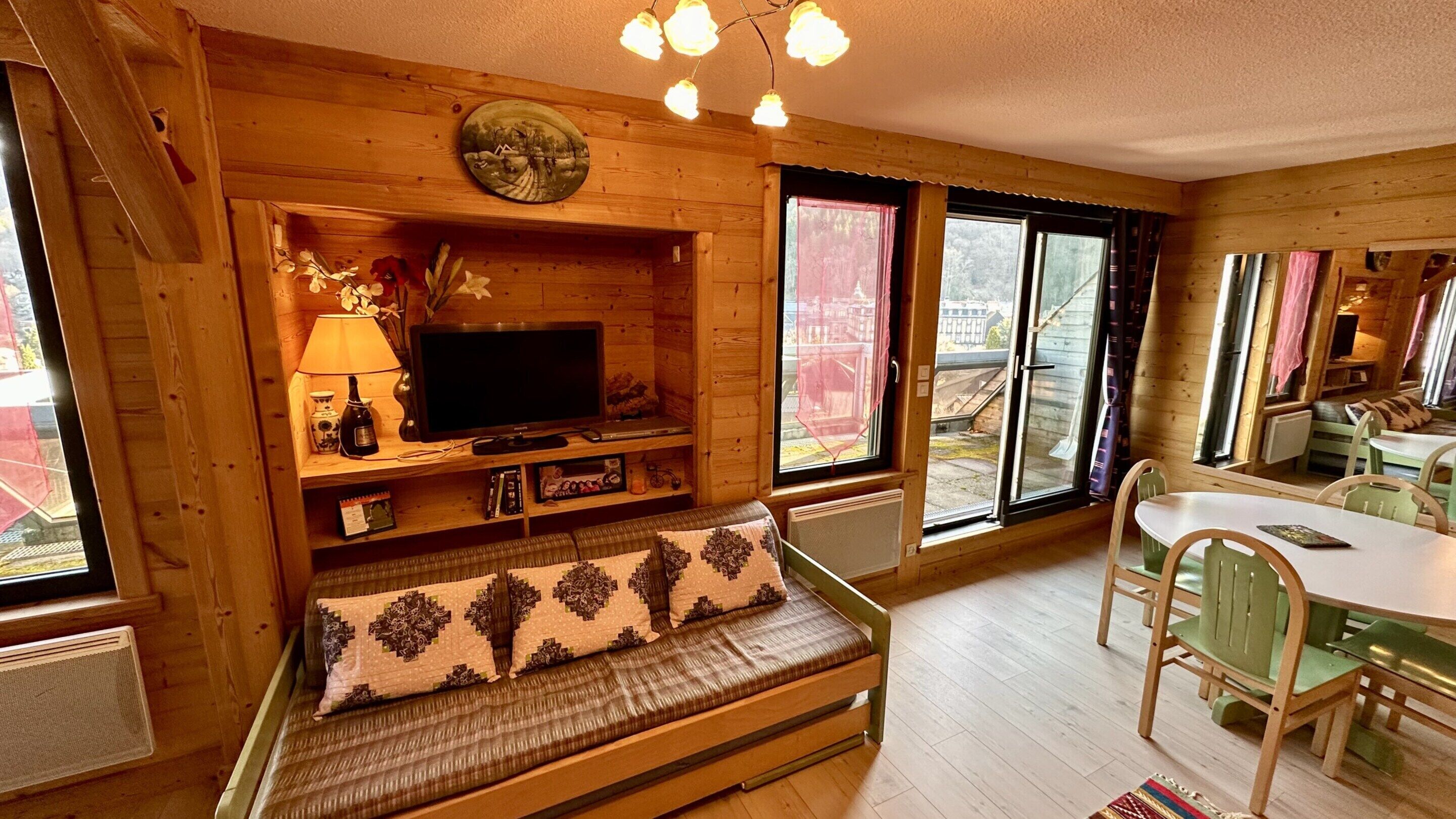 A cozy cabin interior with a wooden bench, a television, and a dining area.