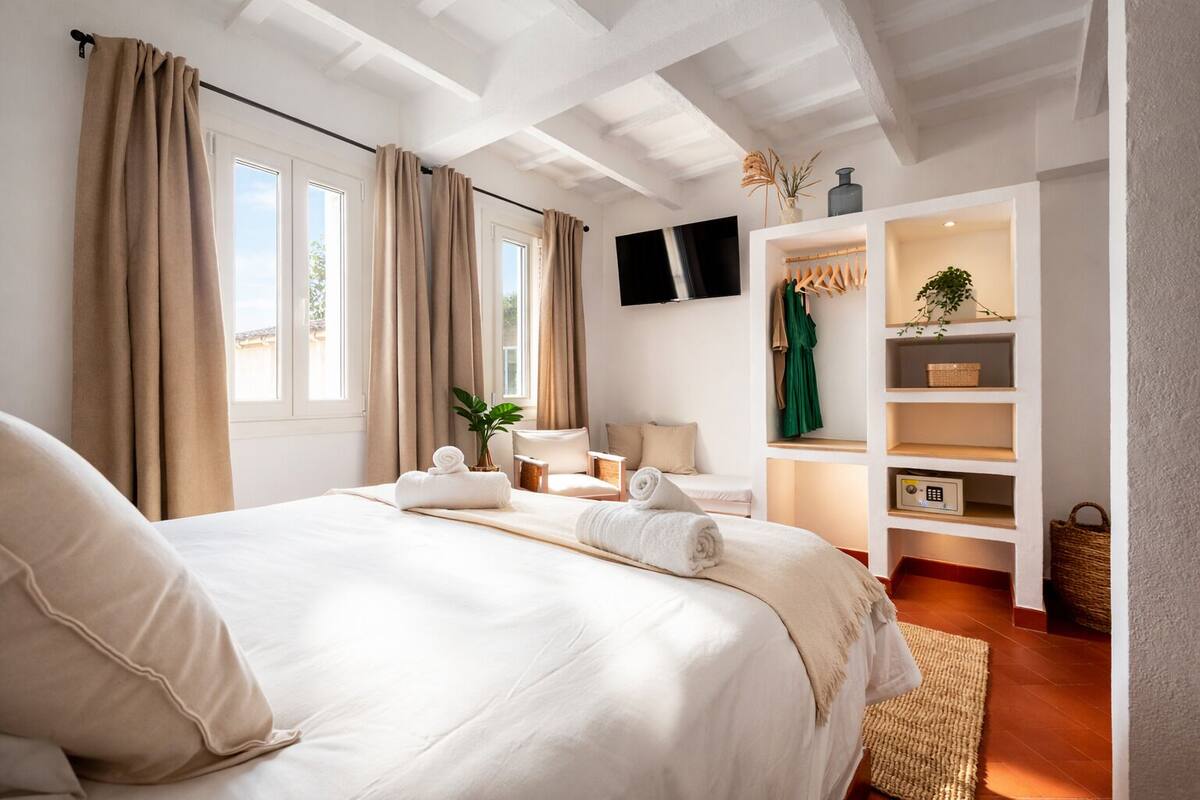 Une chambre d’hôtel dotée d’un grand lit, d’un téléviseur fixé au mur, d’un coin salon avec une table et des chaises, ainsi que d’une bibliothèque intégrée contenant divers objets.