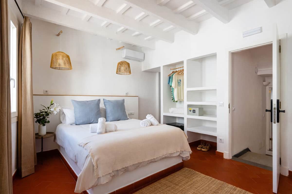 Une chambre d’hôtel comprenant un lit, une armoire, une table de chevet avec une plante et un luminaire suspendu.