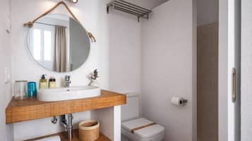 Een badkamer met een ronde spiegel, houten wastafelmeubel, witte wastafel, toilet en een handdoekhouder.