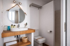 Une salle de bain avec un miroir rond, un meuble-lavabo en bois, un lavabo blanc, des toilettes et un porte-serviettes.