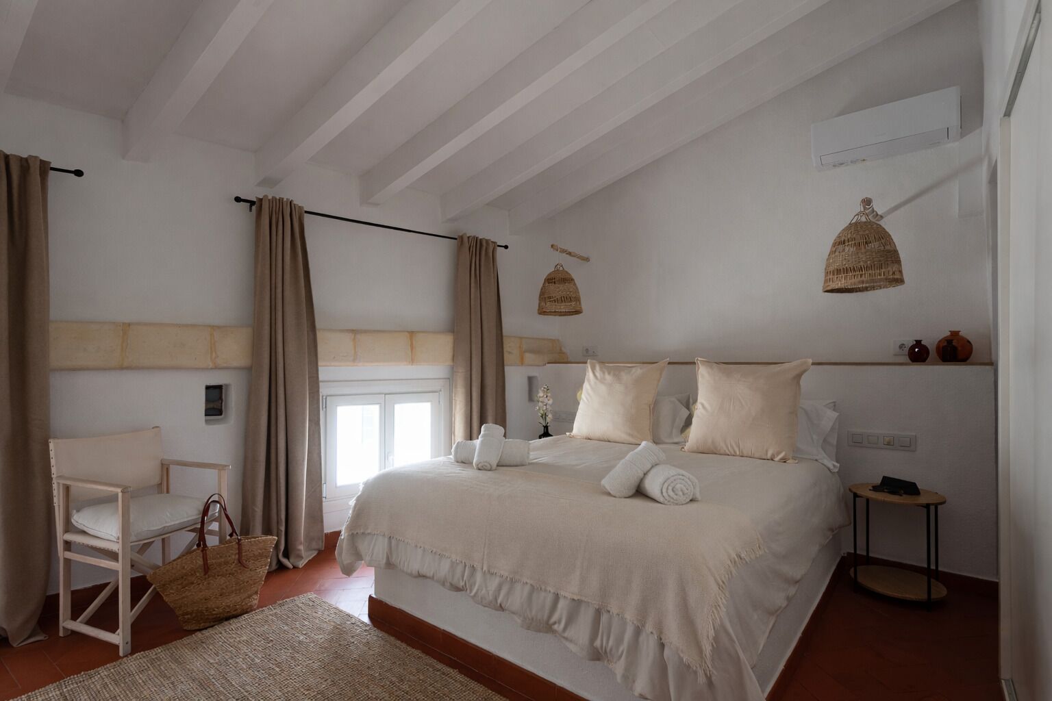 Une chambre à coucher avec un grand lit, une chaise, une petite table et un luminaire suspendu.