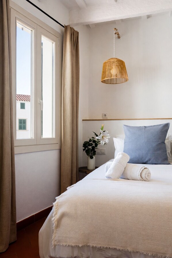 A hotel room with a bed, a hanging light fixture, a window with curtains, and a small table with a vase of flowers. - Hotel Boutique Ses Penyes (Alayor)