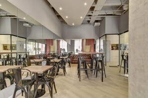 Una sala da pranzo moderna con tavoli, sedie, un divano e un angolo cottura sullo sfondo.
