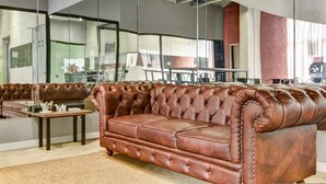 A spacious lobby with a large brown leather sofa, a small wooden table, and a glass partition. - w Inviting Loft w Balcony in Usaquen (Bogotá)