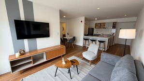 A modern living room with a large flat-screen TV, a grey sofa, a wooden console table, and a small round table with a remote control. - w Chic Inviting 2BR w Balcony in Miraflores (Lima)