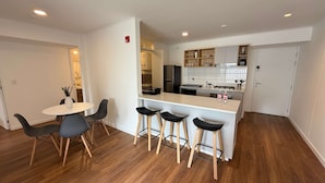 A modern kitchen with white cabinets, a central island with stools, and a dining area with a round table and chairs. - w Chic Inviting 2BR w Balcony in Miraflores (Lima)