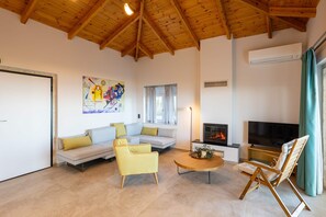 Una sala de estar con techo de madera, un sofá, un sillón amarillo, una mesa de centro, un televisor y una chimenea.