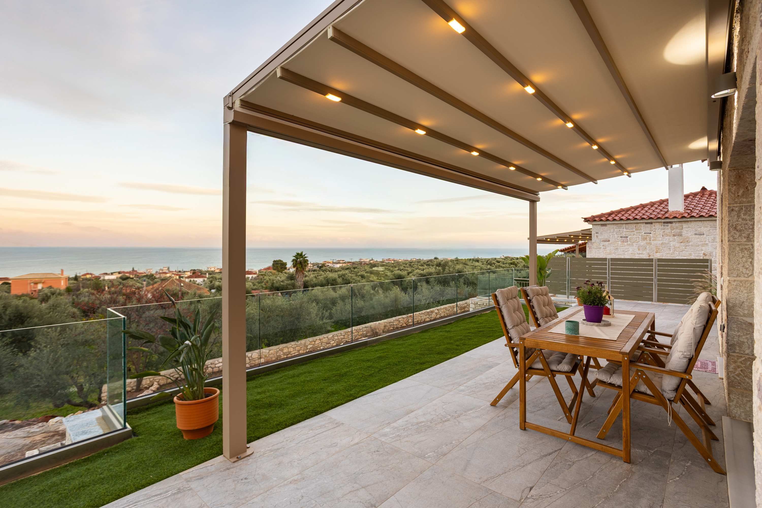 Una terraza con una mesa, sillas, una planta en maceta y vistas al mar y al pueblo.