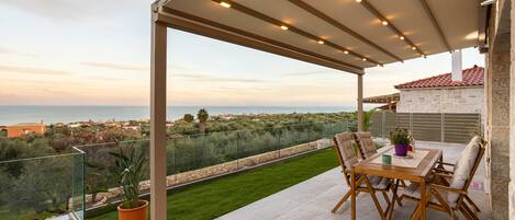 Una terraza con una mesa, sillas, una planta en maceta y vistas al mar y al pueblo.