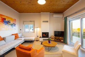 Ein modernes Wohnzimmer mit Kamin, Sofa, Sessel und einem großen Fenster mit Vorhängen.