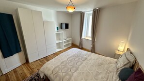 Une chambre à coucher avec un lit, une armoire, une télévision et une fenêtre avec des rideaux.
