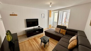 A modern living room with a flat-screen TV, a dark-colored sofa, a small coffee table, and a wooden floor. - Lush Sanctuary Near Forest (Mont-Dore)