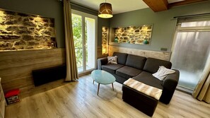 Un salón acogedor con pared de piedra, un sofá, una mesa de centro de vidrio y una lámpara colgante.