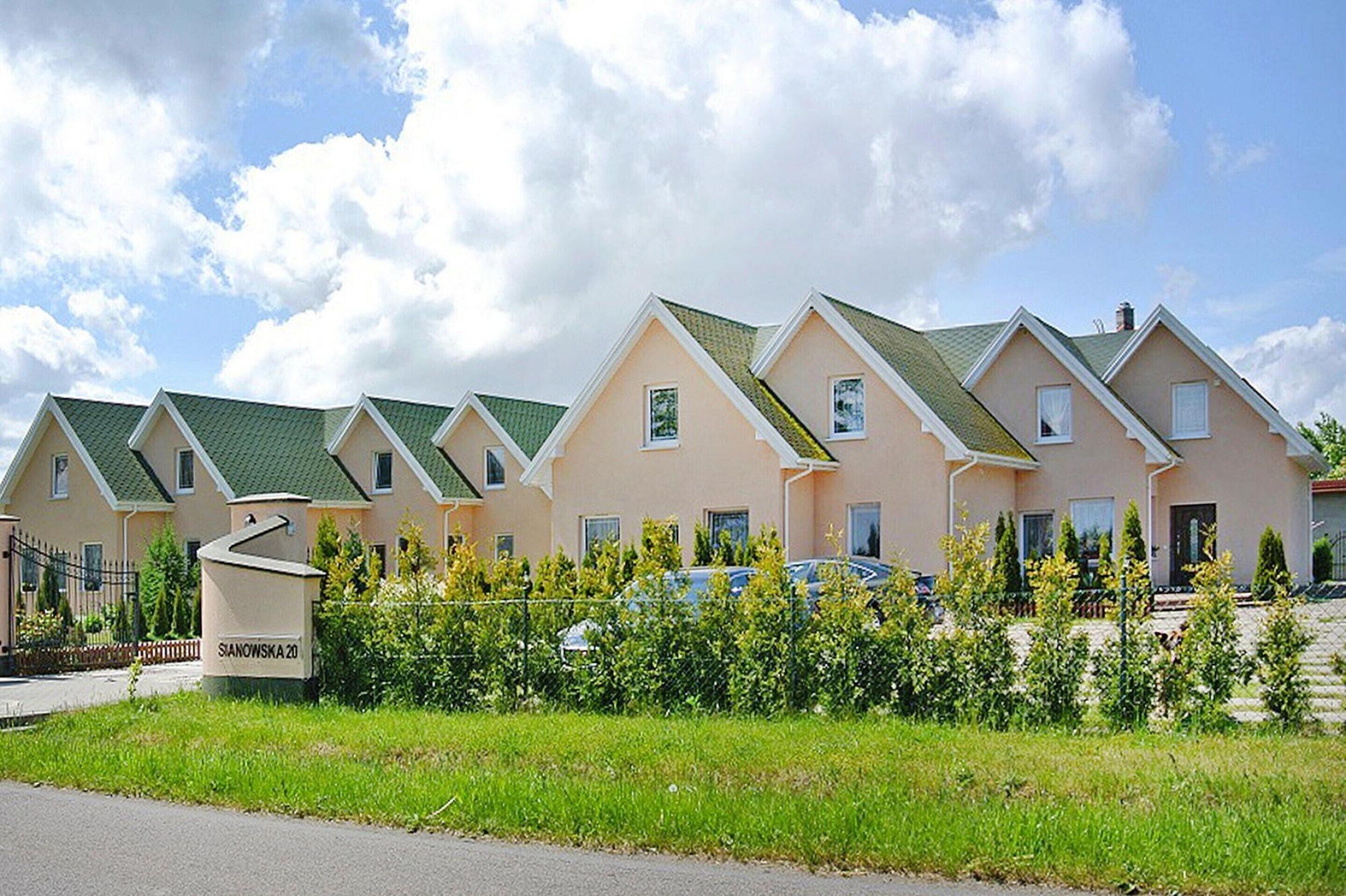 Une rangée de maisons modernes à deux étages, dotées de toits végétalisés et de murs de couleur beige, entourées de verdure et baignées par un ciel dégagé.
