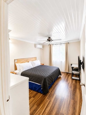 A bedroom with a bed, a ceiling fan, a TV, and a window with curtains. - 202 Batts Rock Beach Condos 1 Bedroom Suite (Bridgetown)