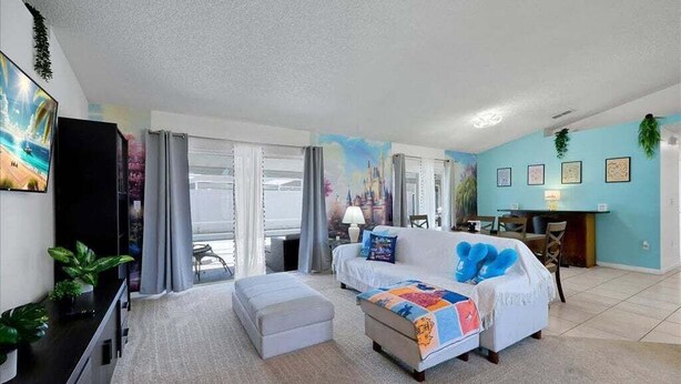 A living room with a sofa, ottoman, and a TV. There is a dining area with a table and chairs. - Minutes to Disney | Cozy 3BR Florida Escape (Kissimmee)