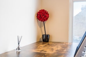 A corner of a room with a wooden table, a black vase with a red flower, and a glass candle holder. - Oxford Cowley city resort with parking and family friendly (Oxford)