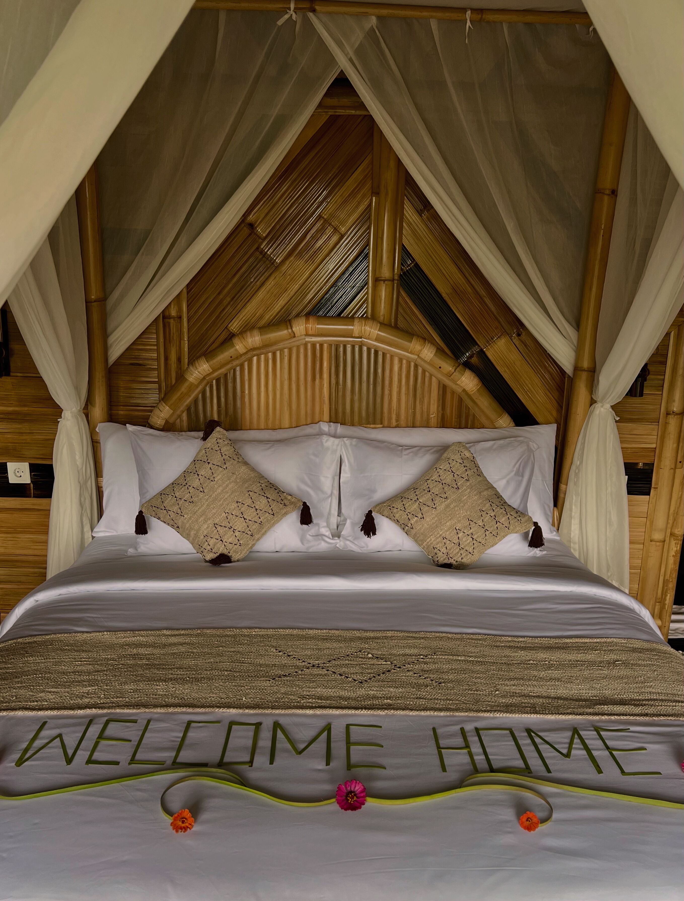 Een bed met hemelbed, witte beddengoed en een bordje met de tekst 'WELCOME HOME'.