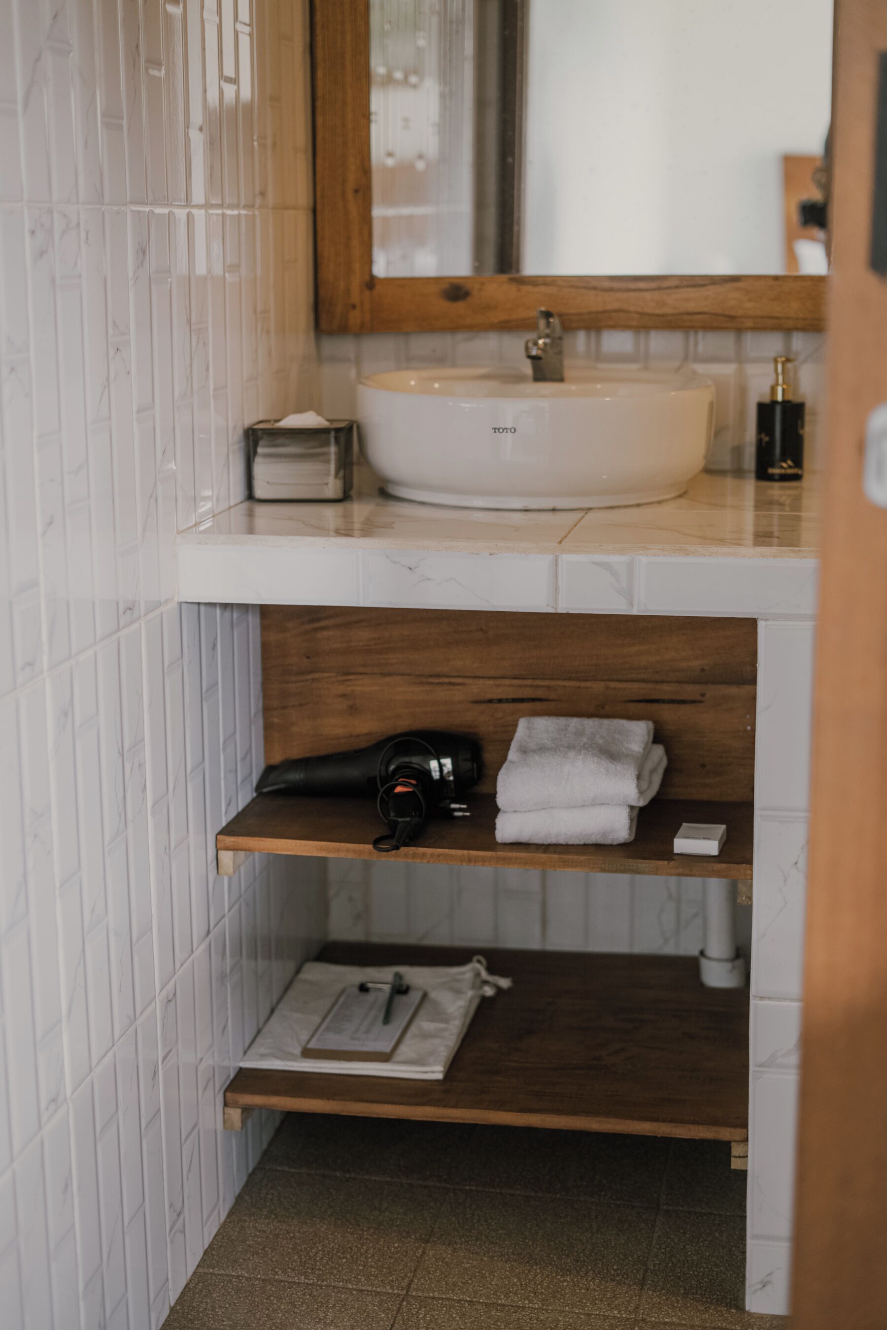 A bathroom with a white sink, wooden shelves, a towel rack, and a mirror.